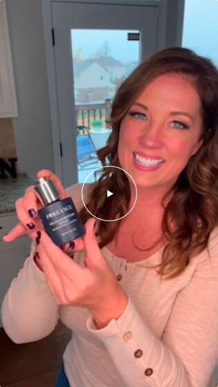 A woman with wavy brown hair is smiling and holding Cellular Restore Serum product