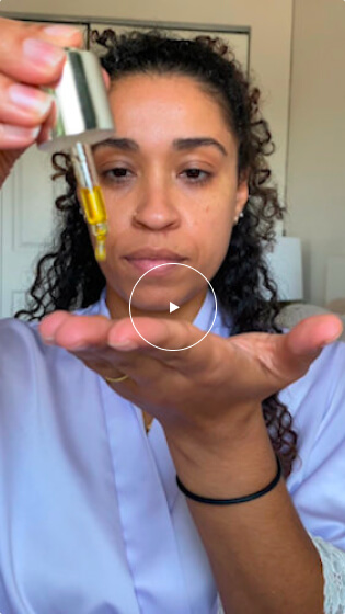 A woman with curly hair dispenses Cellular Restore serum from a dropper bottle into her palm