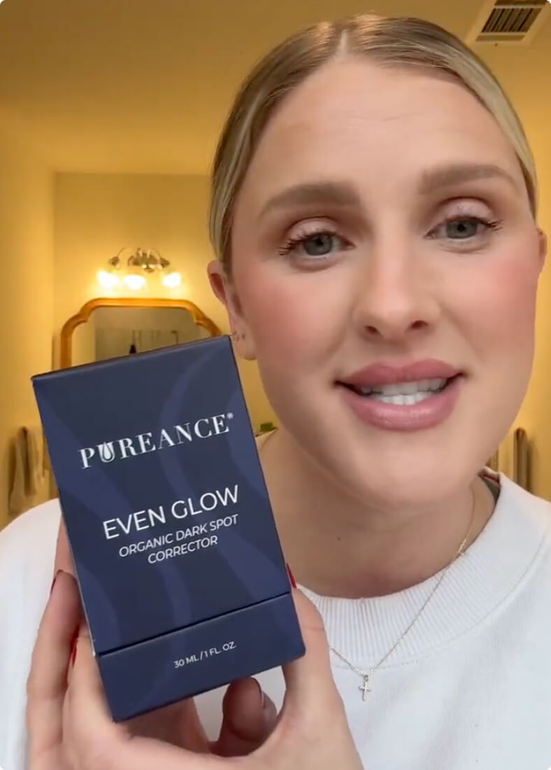 A blonde woman smiles while holding a dark blue box of Pureance Even Glow.