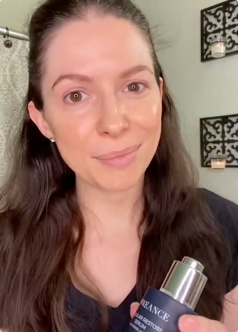 A woman with long dark hair holds a bottle of Pureance Cellular Restore Serum.